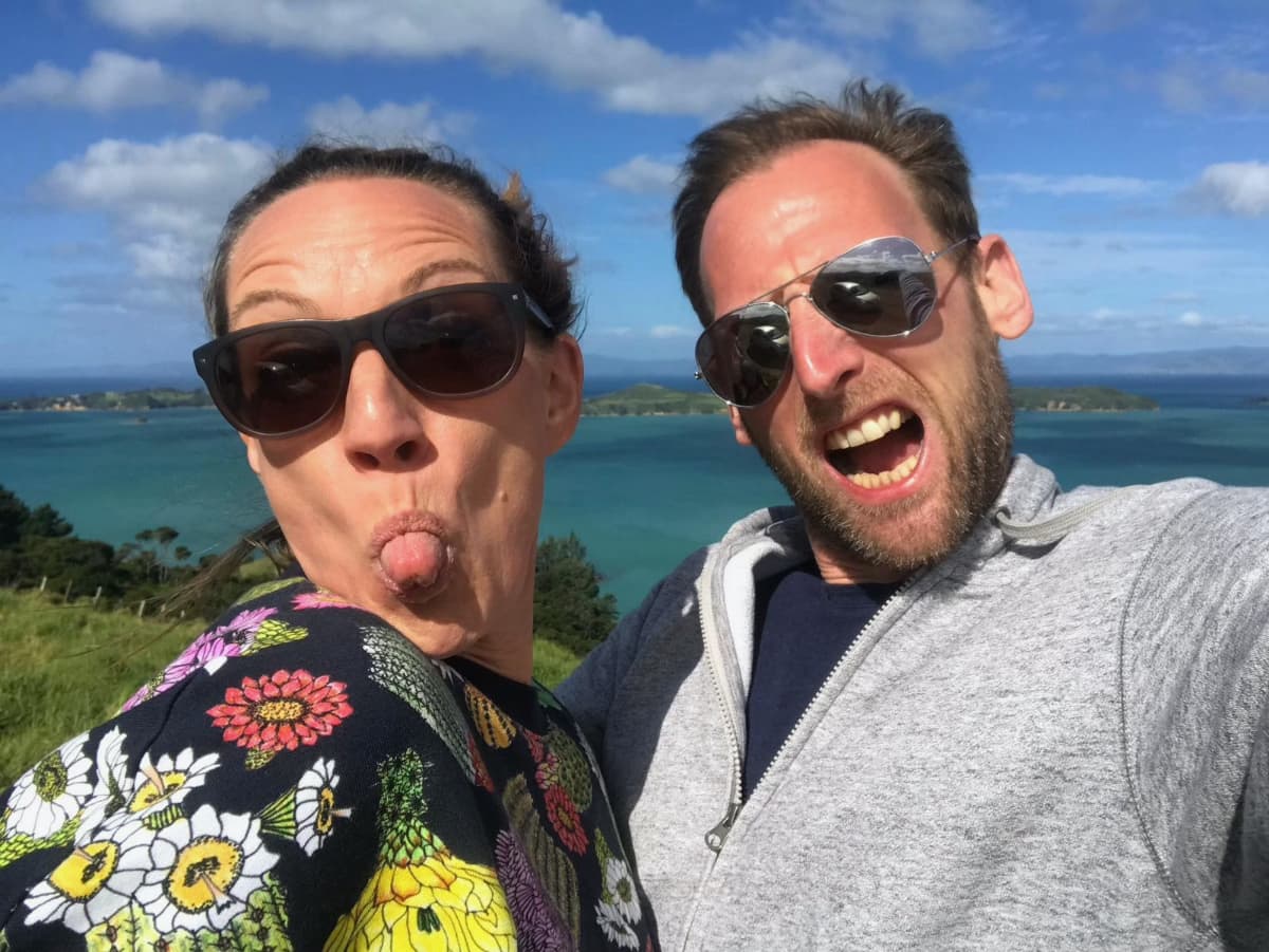 Jane & Holger being goofy on Waiheke Island in New Zealand. Below in the background you can see the tourquoise water of the ocean.